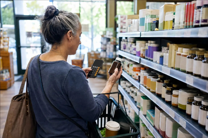 Adult comparing a guarana supplement label with a phone calculator in a wellness aisle