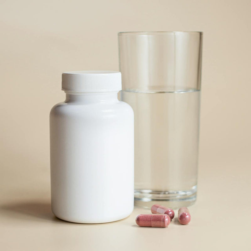 A white supplement bottle beside a glass of water, chelated magnesium glycinate